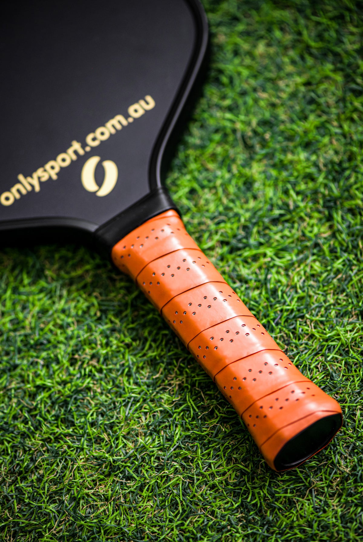 Photo of the grip on the black paddle, laying on the artificial turf