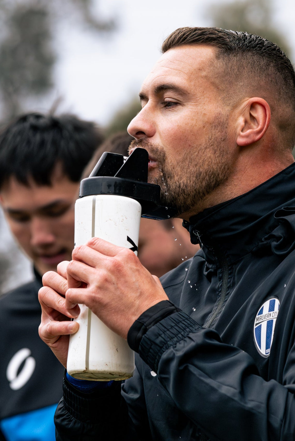 Man in black jacket drinking from a sports water bottle