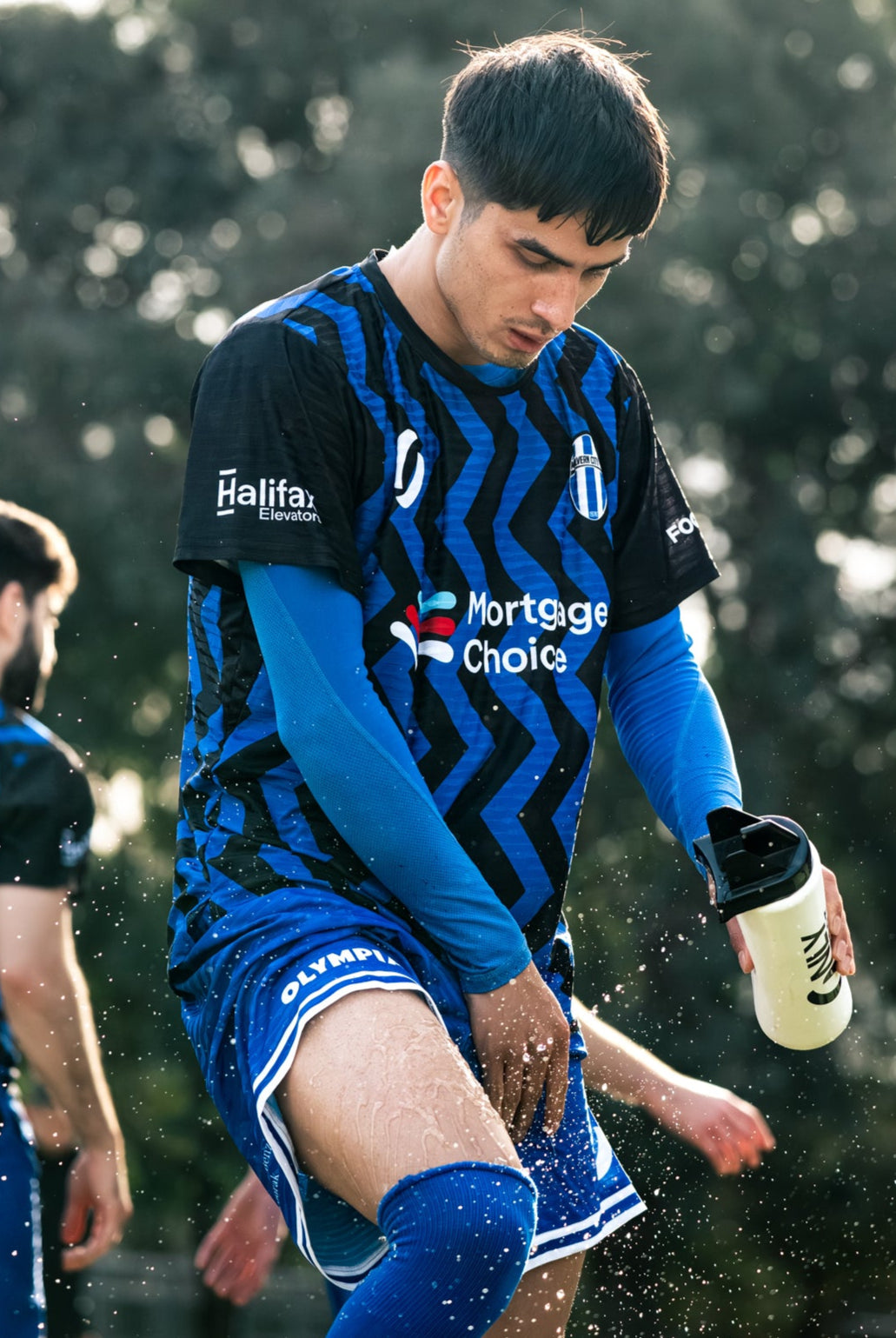 Soccer player in blue uniform spraying water on himself with water bottle