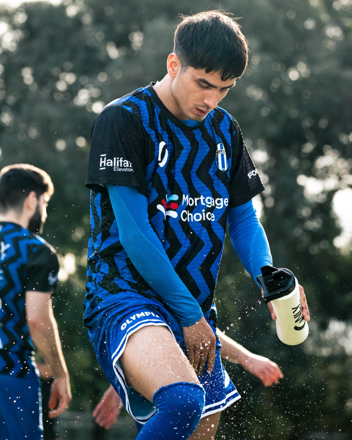 Soccer player in blue uniform spraying water on himself with water bottle