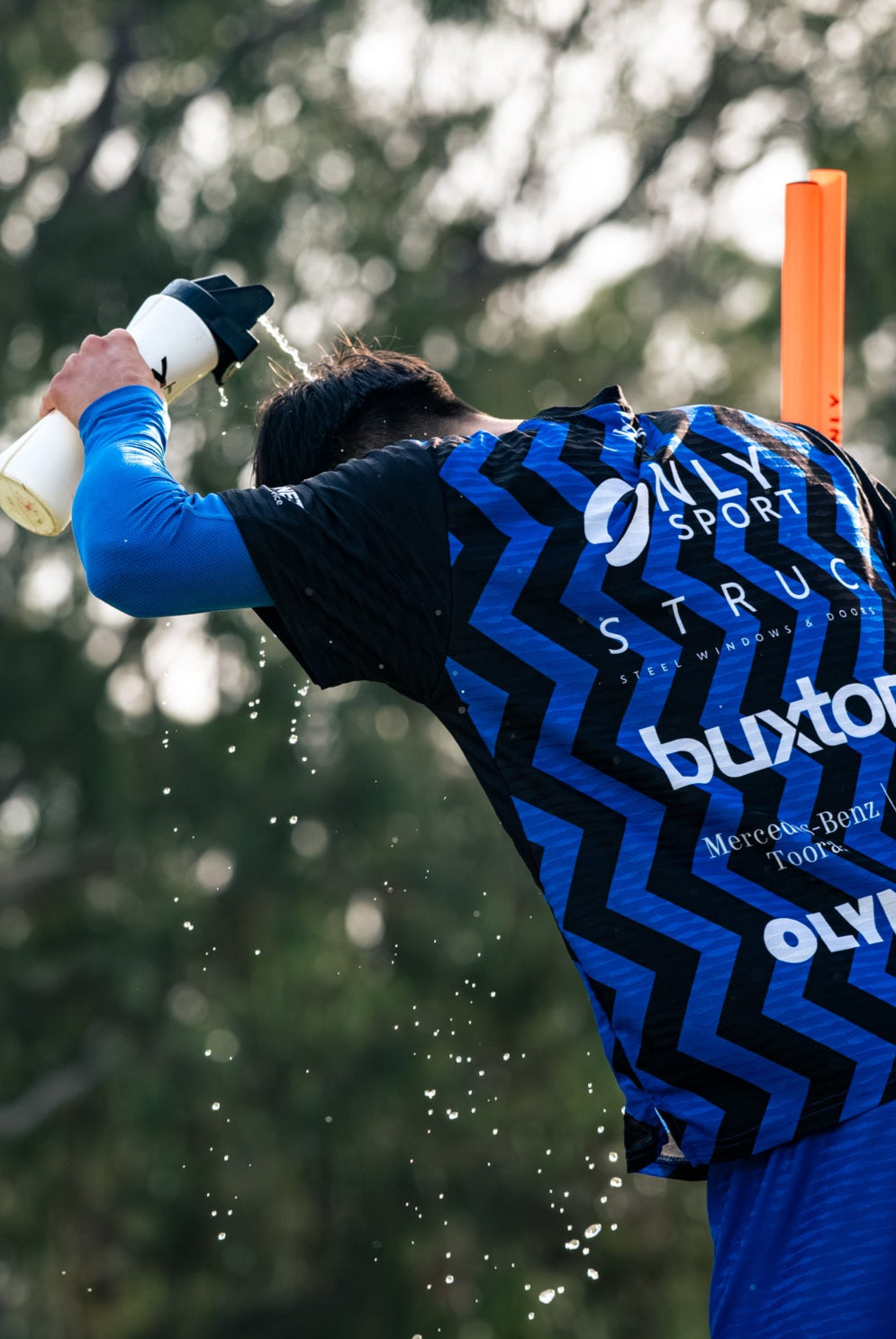 Soccer player in a blue sports jersey spraying water on himself with a water bottle