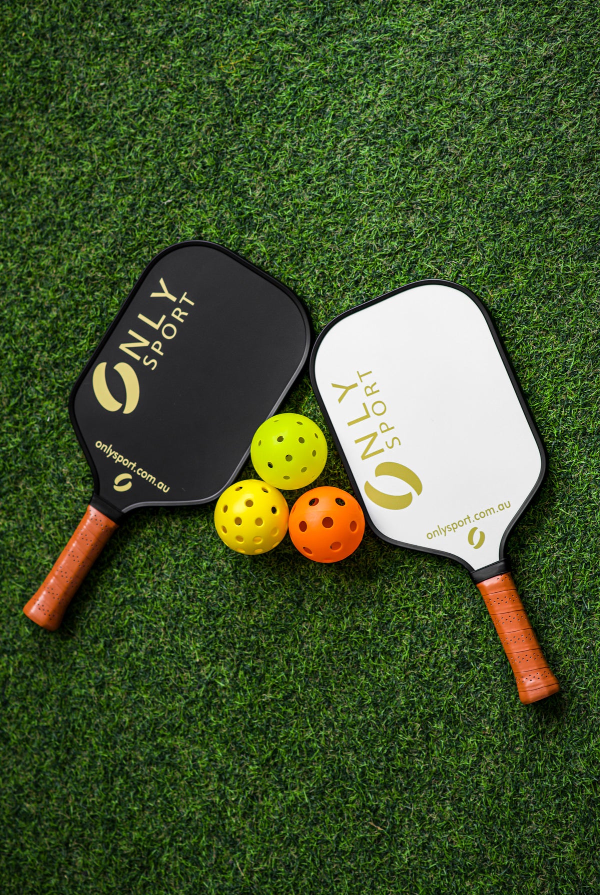 White paddle next to black paddle and three balls laying on the artificial turf