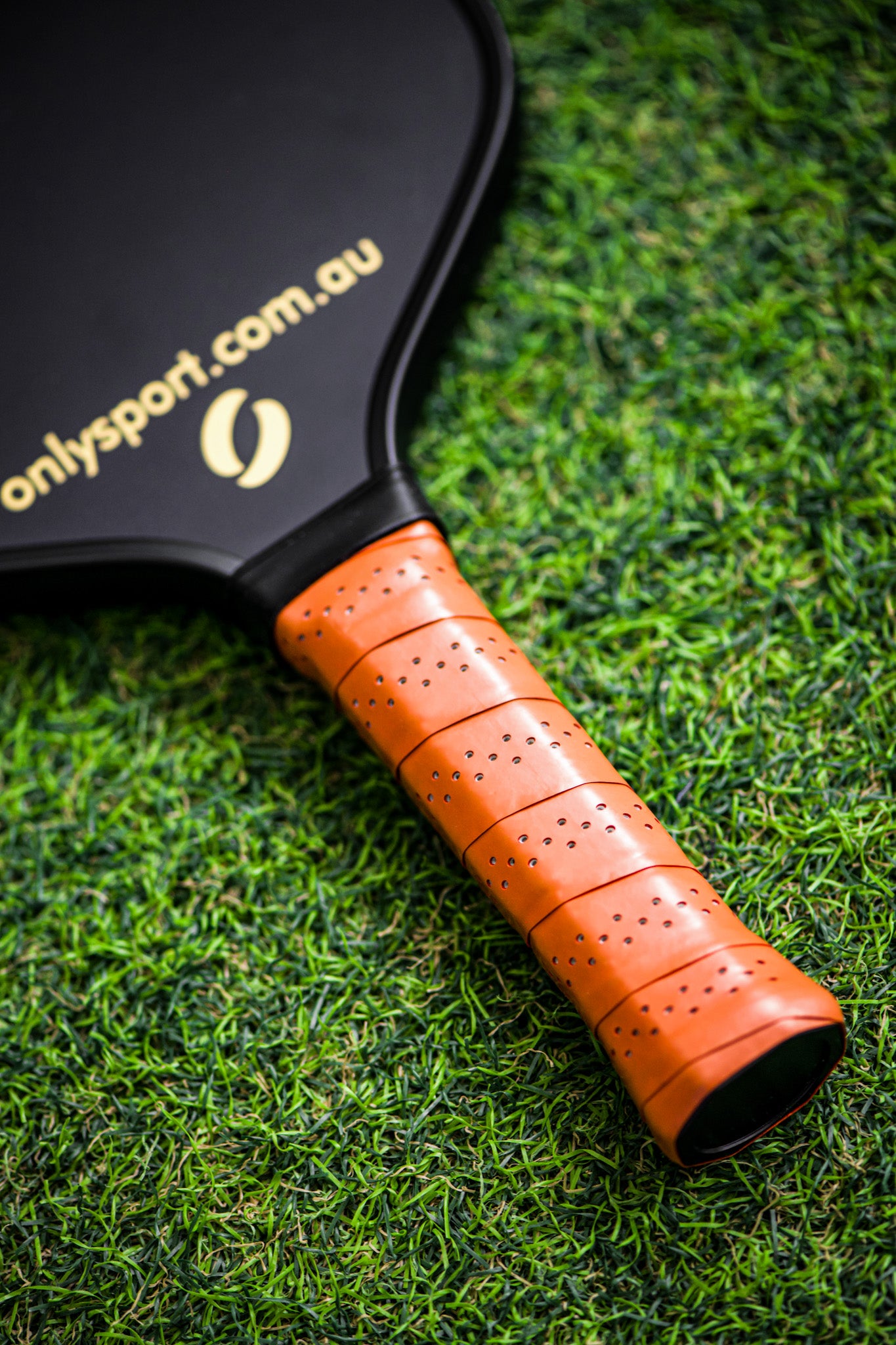 Photo of the grip on the black paddle, laying on the artificial turf