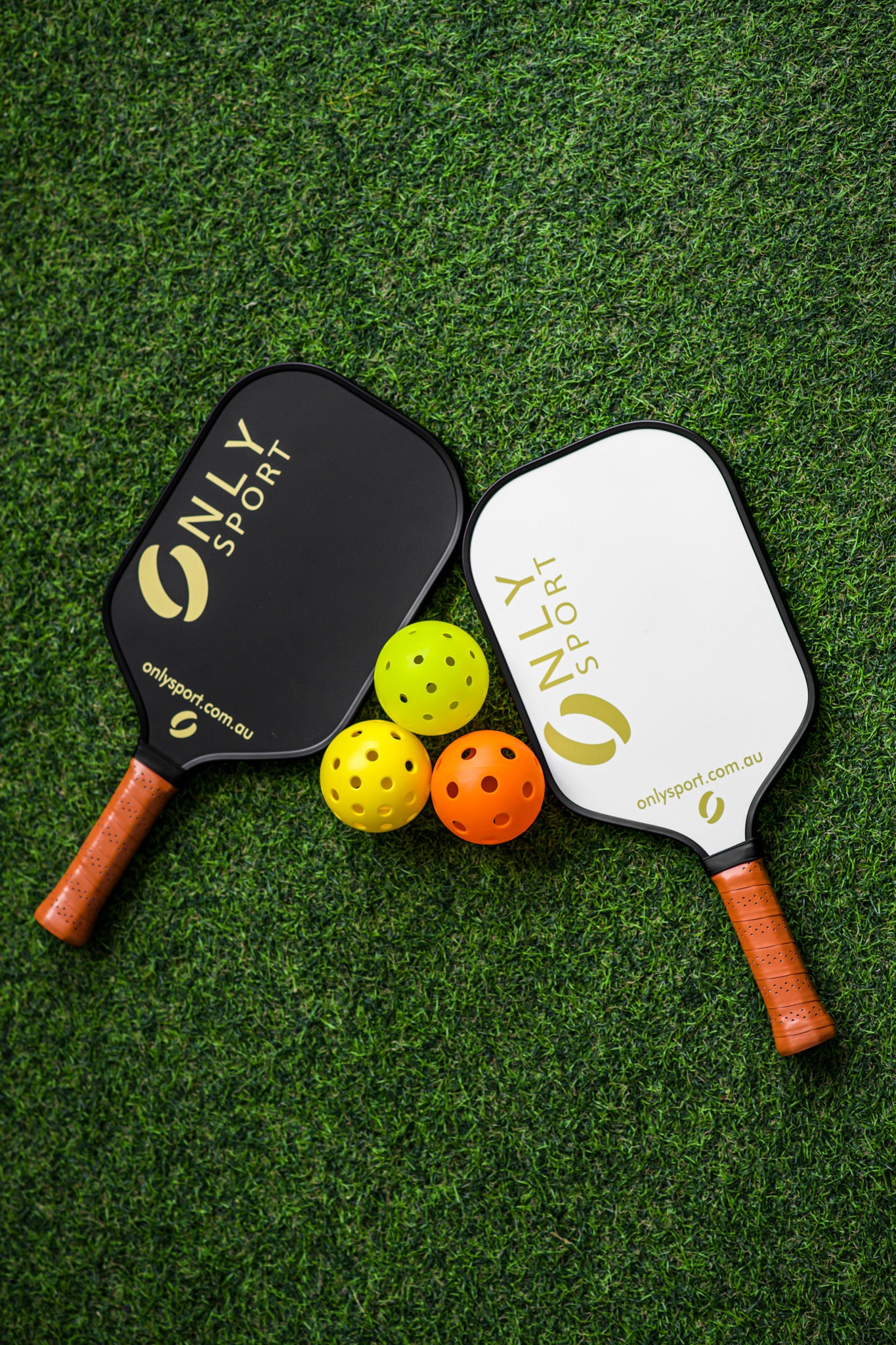 Black and white paddles aligned with three balls, laying on the artificial turf
