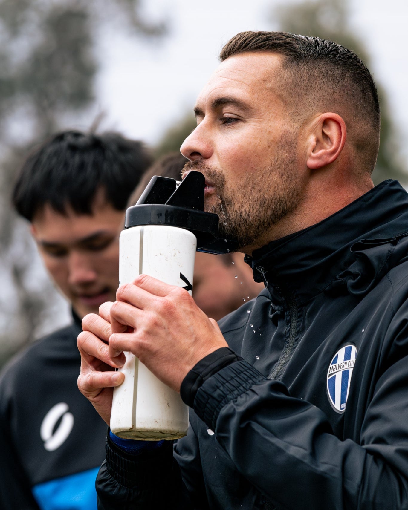 Man in black jacket drinking from a sports water bottle