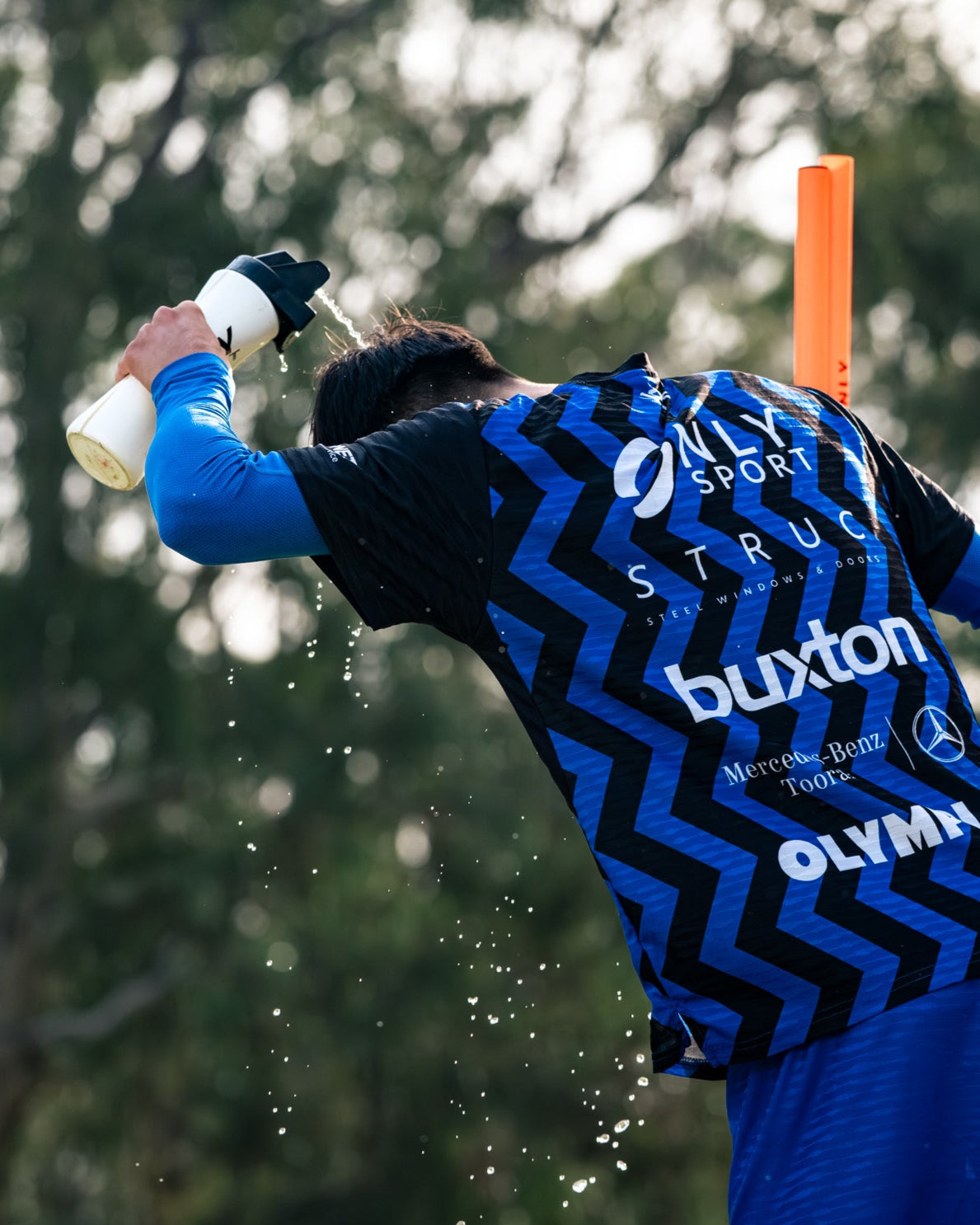 Soccer player in a blue sports jersey spraying water on himself with a water bottle