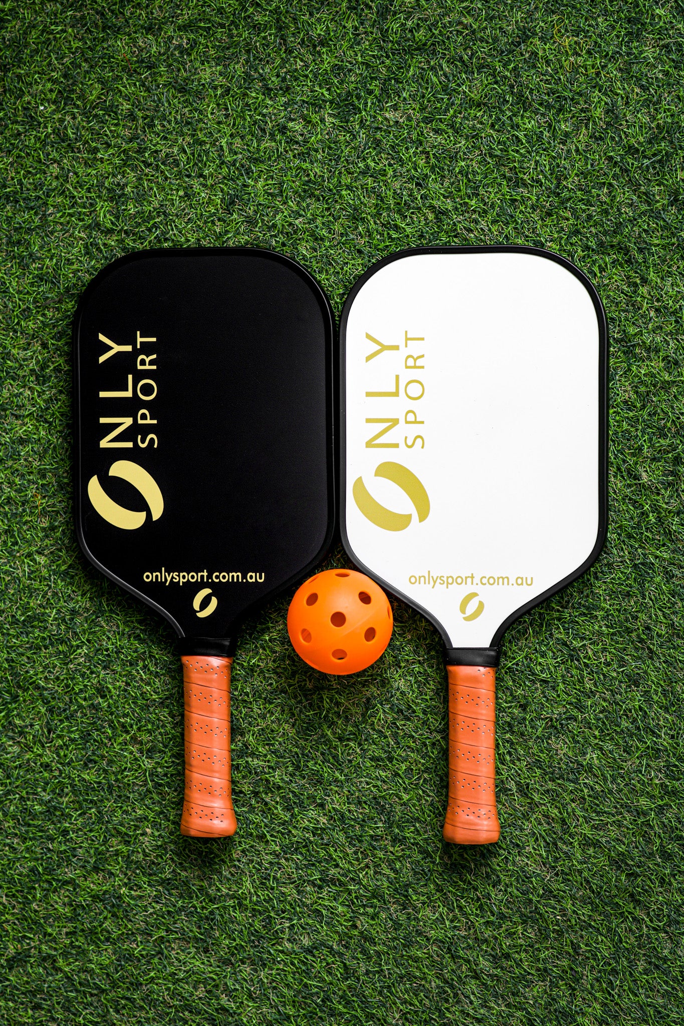 White paddle next to black paddle and ball laying on the artificial turf