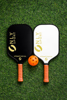 White paddle next to black paddle and ball laying on the artificial turf