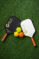 White paddle next to black paddle and three balls laying on the artificial turf